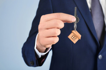 Real estate agent holding key to new house on grey background