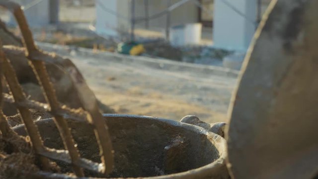 Young white worker pours water into a concrete mixer, closeup, slow motion.