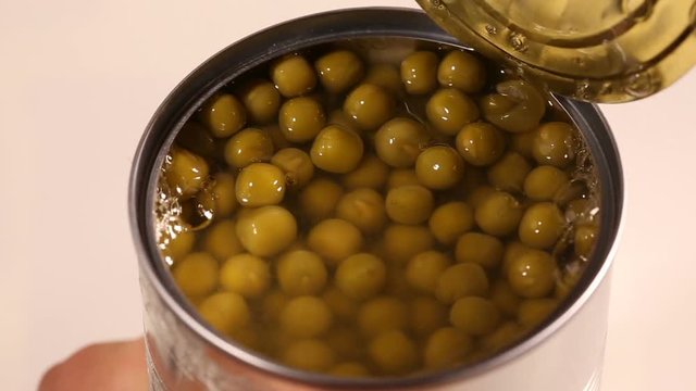 Opening tin can of preserved green peas with hand