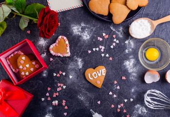 Obraz na płótnie Canvas Homemade cookies in shape of heart with Love word as gift for lover on Valentine's day. Dark stone background with ingredients, flower and decor. Love gift concept. Selective focus. Copy space
