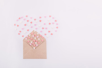 Pink, red and white sweets sugar candy hearts fly out in the form of heart from craft paper envelope on the white background . Valentine day concept. Gift for lover. Selective focus. Space for text.