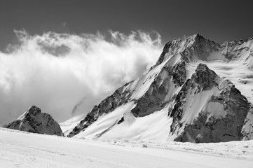 Black and white view on snowy sunlight mountains in clouds