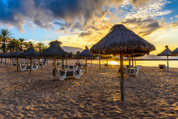 Sunrise view of beach Playa Del Caminson with sun loungers and umbrellas at sunrise, Playa de la Americas on Tenerife, Canary Islands in Spain