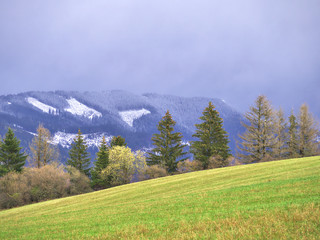 Late autumn in Slovakian mountain valley. Fields are still green but snow falls on the higher peaks.