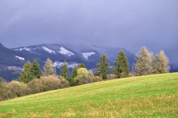 Late autumn in Slovakian mountain valley. Fields are still green but snow falls on the higher peaks.