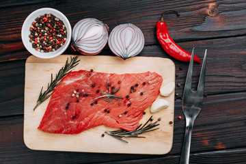 Raw meat, beef steak with rosemary, vegetables and spices flat lay on wooden board, kitchen, cooking concept