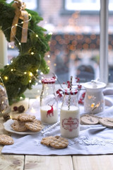 Fototapeta na wymiar girl milk in a glass at the table by the window, cookies on a plate, and a wreath of Christmas tree