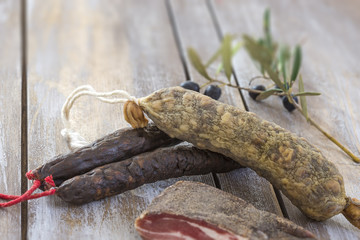 several variety of traditional Corsican charcuterie with an olive branch and black olives on wooden background