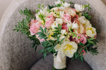 Bridal morning details. Wedding bouquet of yellow, beige and pink flowers with greenery on a chair.