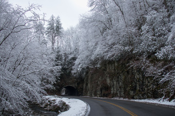 Fototapeta premium Tunnel and curvy windy road and mountain stream through snow covered woods in Great Smoky Mountains National Park