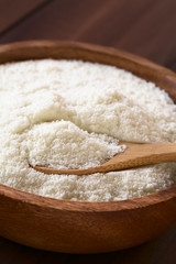 Powdered or dried milk in wooden bowl with small wooden spoon, photographed with natural light (Selective Focus, Focus on the milk powder on the spoon)