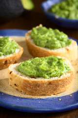 Fresh avocado cream or guacamole on onion bread slices, photographed with natural light (Selective Focus, Focus on the front of the avocado cream on the first bread)