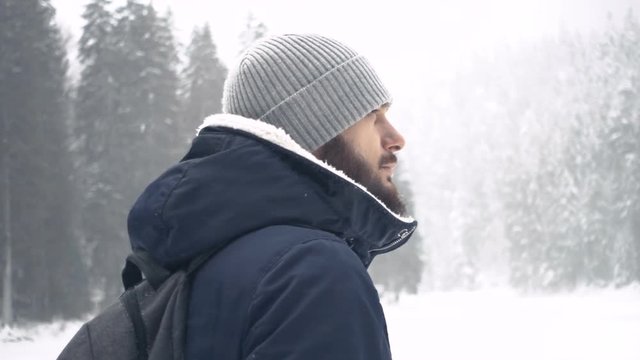 Portrait of cheerful handsome bearded young man standing in winter forest. Slow motion