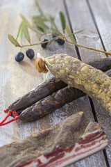 several variety of traditional Corsican charcuterie with an olive branch and black olives on wooden background