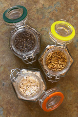 Chia seeds, toasted oat grains and oat flakes in swing top glass jars, photographed overhead on slate with natural light (Selective Focus, Focus on the top of the chia and oats)