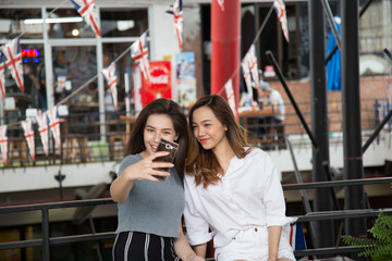 Asia girl and friend ethnic German-Thai taking smart phone selfie in department store.