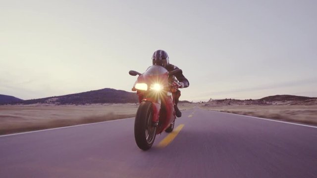 Motorcyclist racing his motorcycle down straight country road going a high speed  at sunset