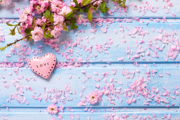 Pink  sakura flowers and  little decorative heart on blue wooden planks.