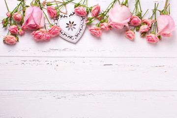 Decorative heart and border from pink roses flowers on white wooden background.