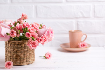 Pink roses flowers  and cup of coffee against  white brick wall.