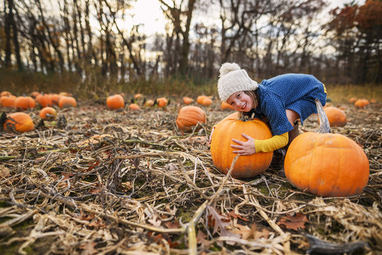 Smiling Girl trying to pick up a heavy pumpkin in a pumpkin patch in autumn, USA