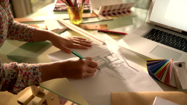view from above, on the hands of an architect drawing a kitchen plan by hand. On his desktop a laptop, color chart and drawing tools