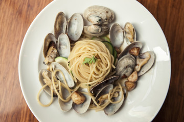 oil pasta with clam on the white dish, wood desk.