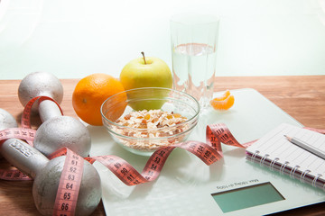 Healthy diet, fitness and weight loss concept. Scales, measuring tape, apple, oatmeal, open notebook and pencil on the table.