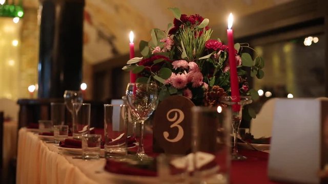 Christmas wedding banquet hall interior details with decorand table setting at restaurant. Winter season decoration of bulb garlands, candles, flowers, cones and fir tree branches