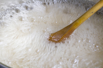 Wooden spoon stirring rapidly boiling liquid close up in cooking pot - Fractal movement texture
