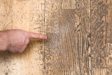 Man's hand pointing to the old scratched wooden floor in the room. Problems and solutions concept.