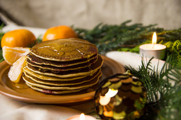 Pancakes with oranges on a Christmas table with candles