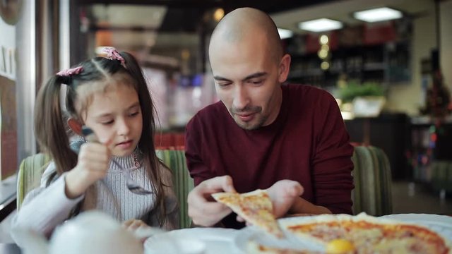 Dad with a small daughter in a pizzeria eating pizza