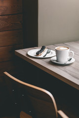 Cup of coffee on wooden table with eclair