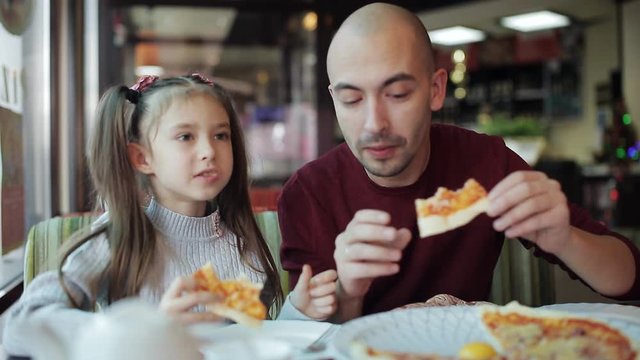 Dad with a little daughter enjoying the taste of fragrant pizza in a pizzeria