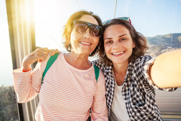 An elderly beautiful woman and her adult daughter travel together, do selfie on a mobile phone in...