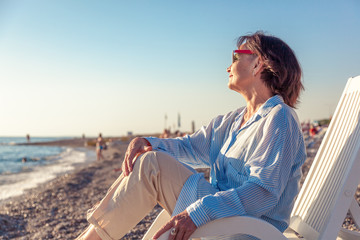 beautiful elderly woman sitting in a deckchair on the beach and admiring the sunset