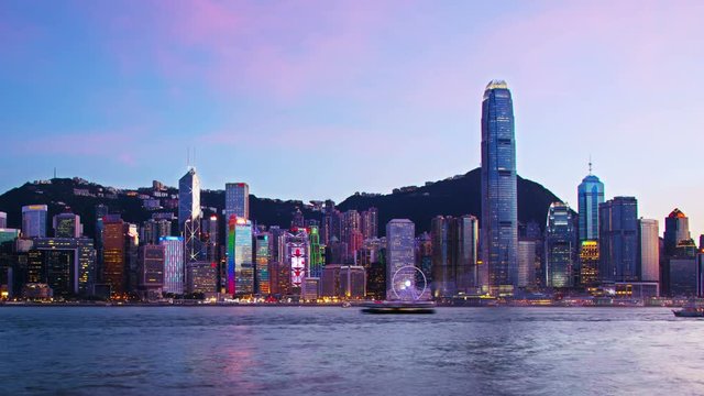 Hong Kong. Skyline of Hong Kong from day to night. Beautiful skyscrapers with sunset sky. Time-lapse of boats at Victoria harbor. Zoom out