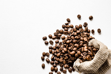 Brown beans with burlap bag on the white table. Harvest of coffee in different countries. Choice of the best sort and quality coffee. Empty place for a text.