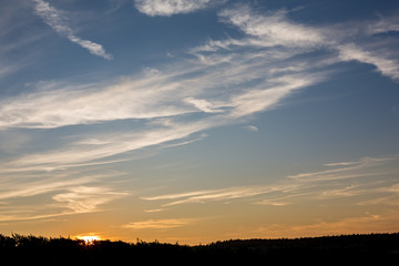 Horizontal cloudscape of layered clouds at sunset with Sun