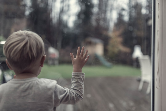 Toddler boy staring out of a window in evening light into the garden