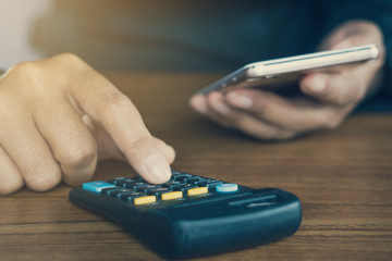 close view of a business man hand calculating his monthly expenses during tax season with calculator and smart phone  on desk 