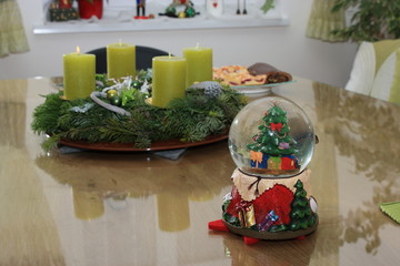 schneekugel mit weihnachtsmotiv vor adventkranz auf tisch