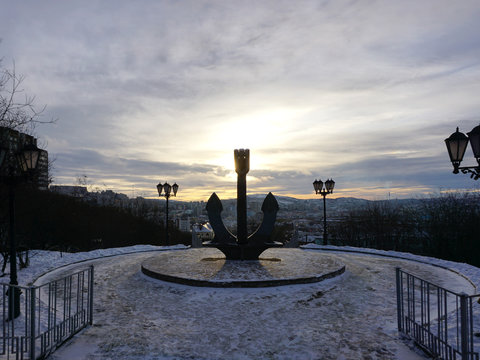 Memorial Metal Anchor With Murmansk City And Sun Rise Background In Murmansk