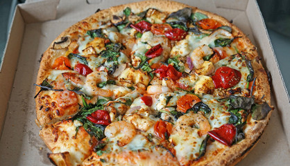 Pizza with shrimps, camembert cheese and cherry tomatoes, served in a pizza box
