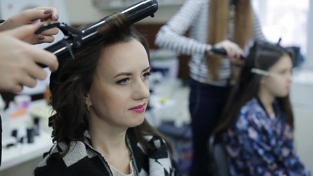 Hairdressing salon. The specialist in hair stacks the girl on a party. The hairdresser does ringlets by means of the special curling iron.