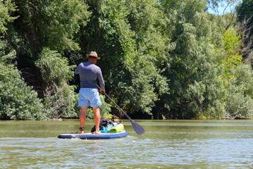 Tourist guy is paddling on SUP ( Stand up paddle board) at Danube river on biosphere reserve in spring. Concept of water tourism
