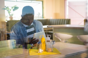 Young man using his tablet while having drink