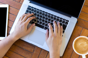 Fototapeta premium Young man hands working on laptop computer placed on wooden desk. Top view
