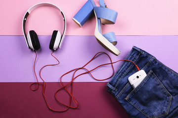 Women's clothing, jeans and headphones on a light violet and lilac background. The view from the top. Flat lay.